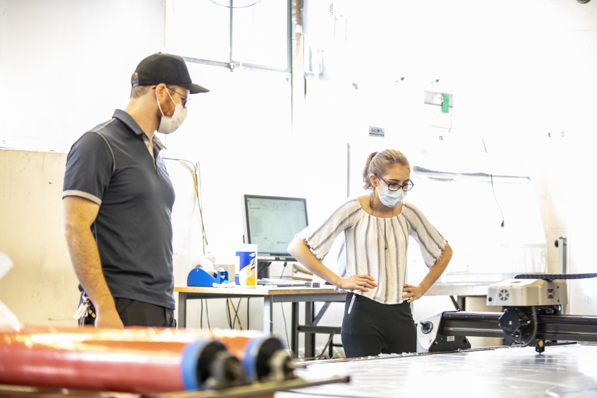 A man and a woman watch a machine cutting plastic sheeting