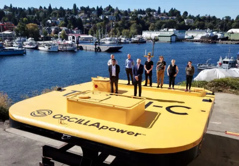 A group of 8 people stand on a large yellow wave energy converter