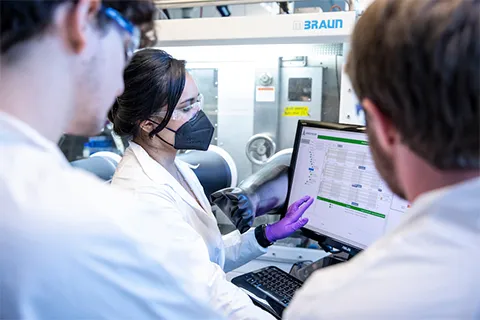 Woman explaining data on a computer to two male students