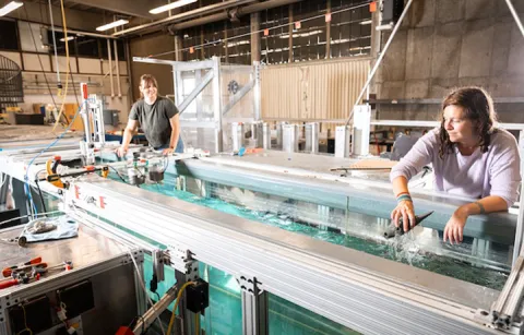 Two women placing a tidal turbine with sensors, along with a silicone whaale model, inside a wave facility at the Harris Hydraulics Lab. 