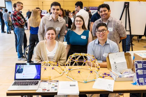 Five people at an exhibition posing for the camera behind a table