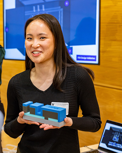 A student smiles and holds a prototype of a laser system tool for scribing solar cells.