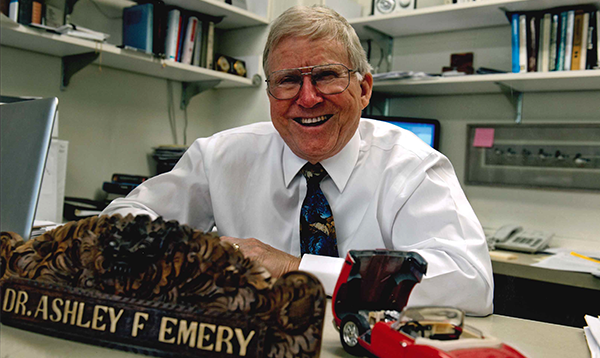 Ashley Emery was sitting behind his desk, which has a sign with his name and a model car on it.