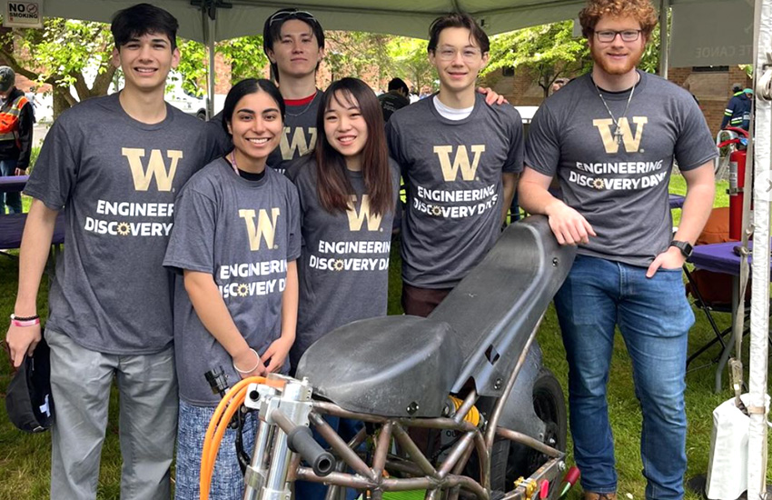 Members of the Washington Superbike team outside wearing Engineering Discovery Days shirts alongside their bike.