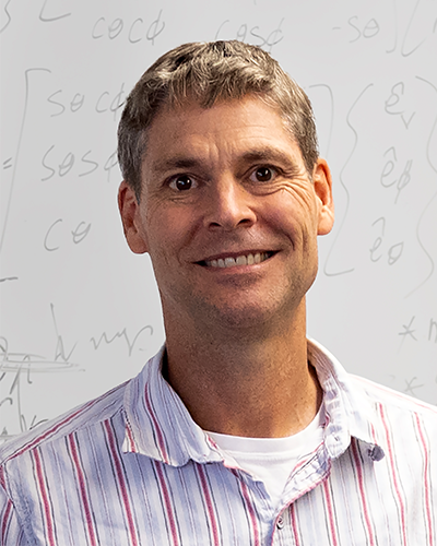 Michael Bailey smiling headshot with a backdrop of equations on a whiteboard