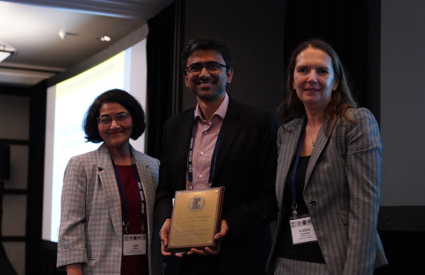 Aniruddh Vashisth is smiling and holding a plaque, standing between two people at the ASC conference.