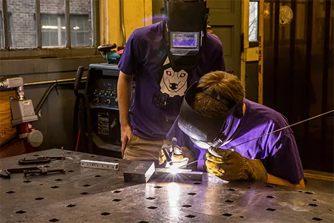 Two students with masks welding in a lab