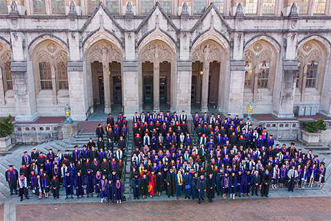 Aerial shot of faculty and students wearing robes standing in front of a building