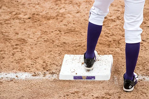 Close-up of a player's feet on a baseball base with a purple "W" mark