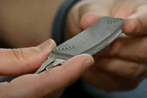 Close-up of hands holding a small, rectangular electronic component with parallel grooves on its surface